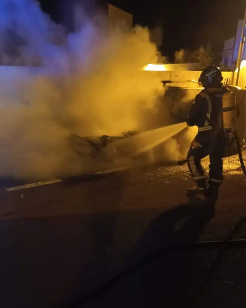 Brandstiftung in Santa Cruz: Vandalen zünden Müllcontainer an Einsatzkräfte der Feuerwehr löschen mit einem Löschschlauch einen in der Nacht brennenden Müllcontainer auf einer Straße in Santa Cruz de Tenerife.